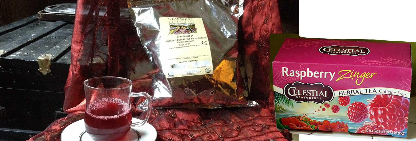 (left) cup of hibiscus tea with foil package of Starwest Botanicals dried hibiscus flowers (right) package Celestial Seasonings Raspberry Zinger herbal tea